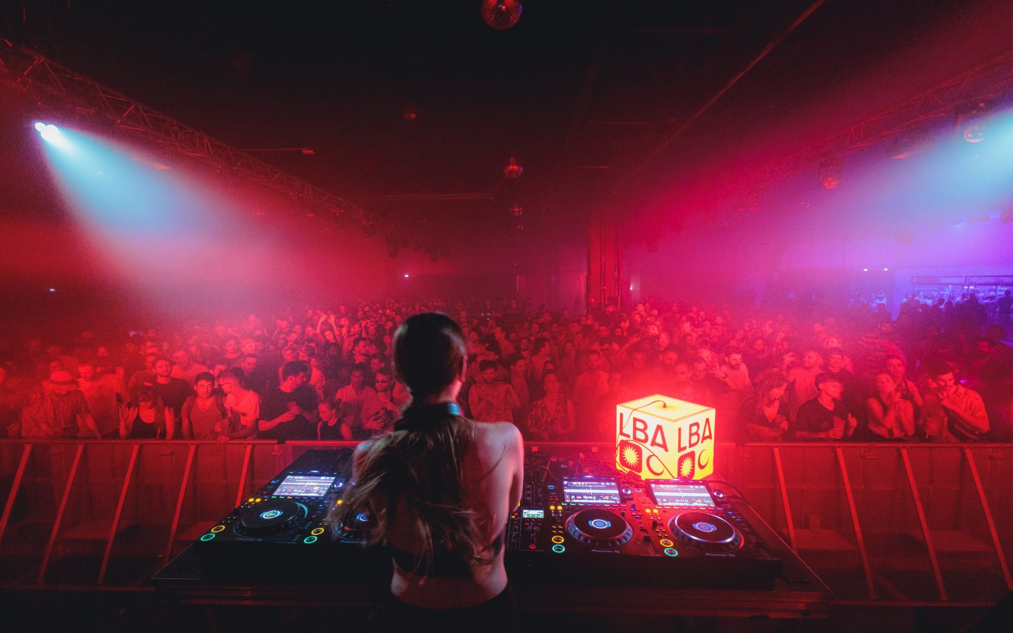 Photographie de nuit derrière un DJ présent au Festival Le Bon Air, avec une foule de spectateurs.